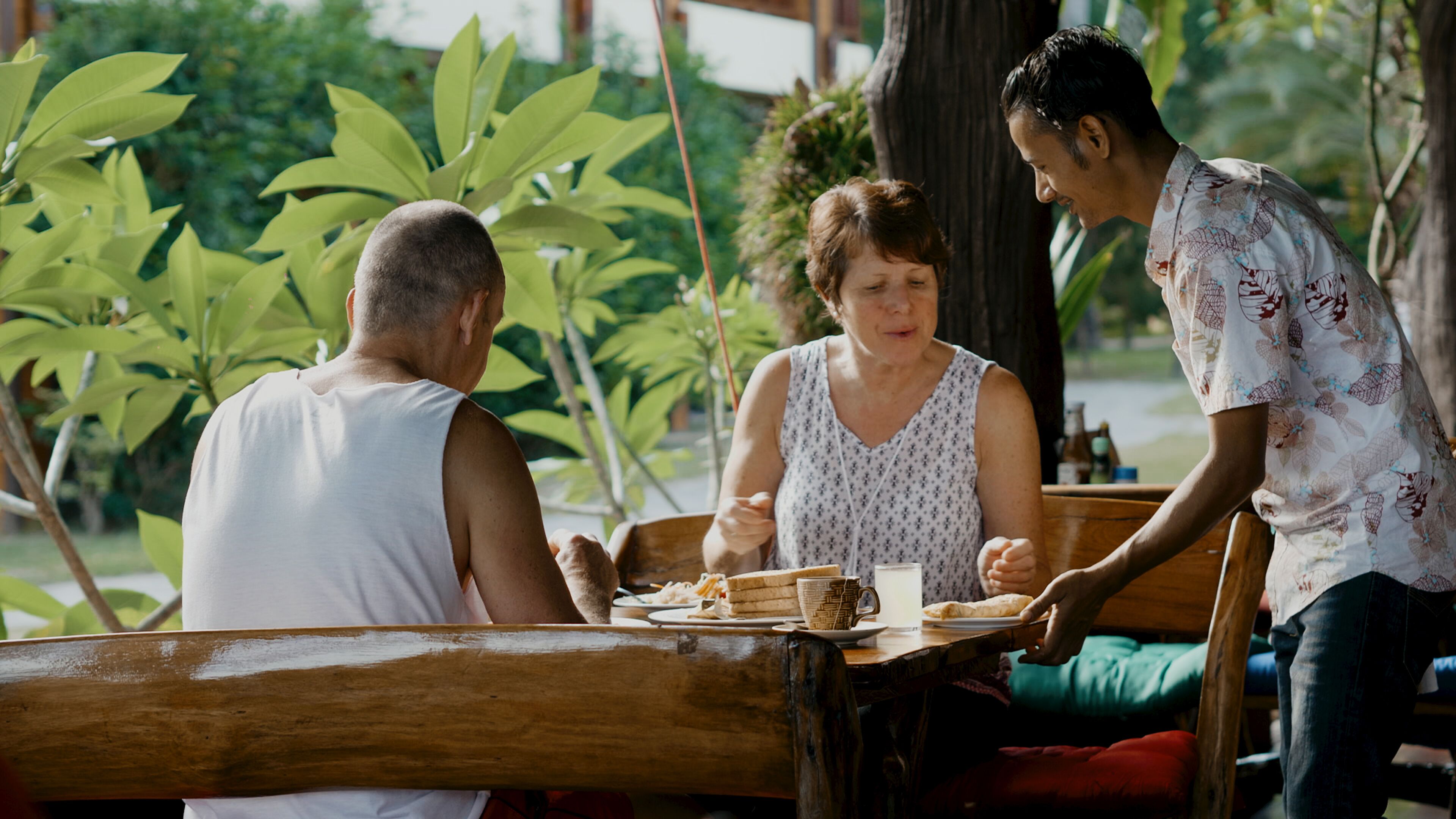 A wooden table with plates of food and a bottle, surrounded by people seated on benches.