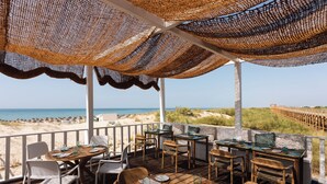 An outdoor dining area with tables and chairs, overlooking a beach.
