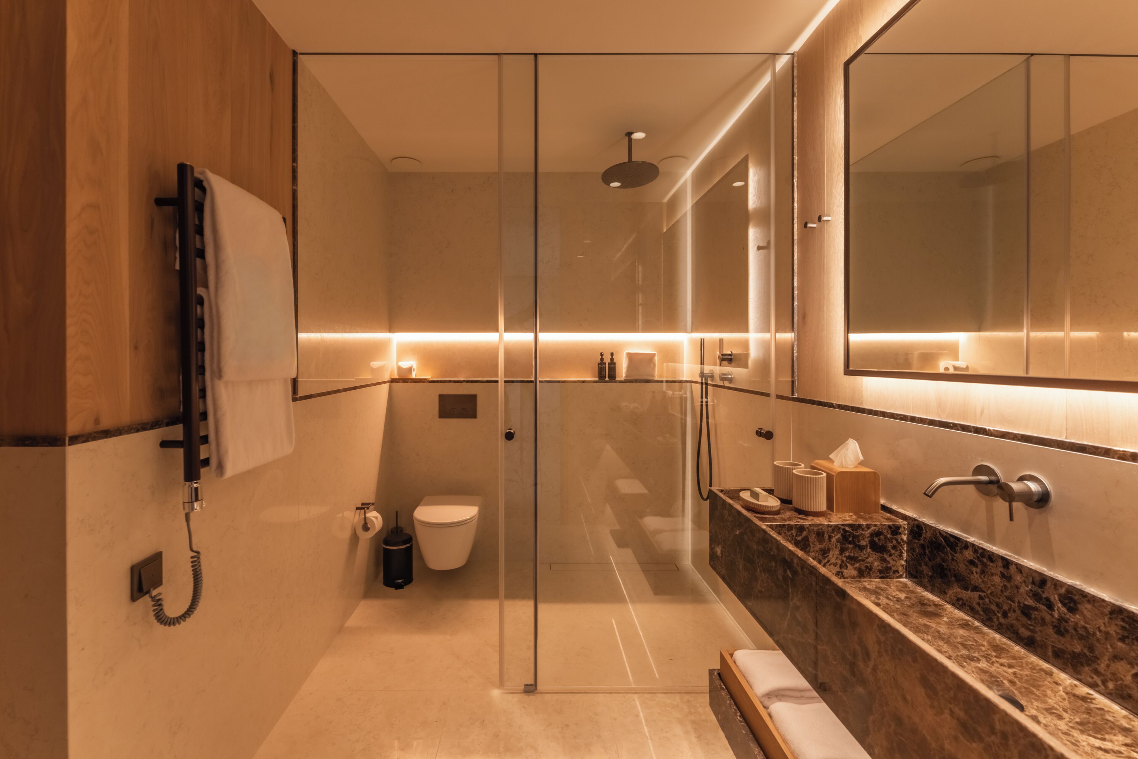 A modern bathroom with a glass shower enclosure, a marble countertop, and a large mirror.