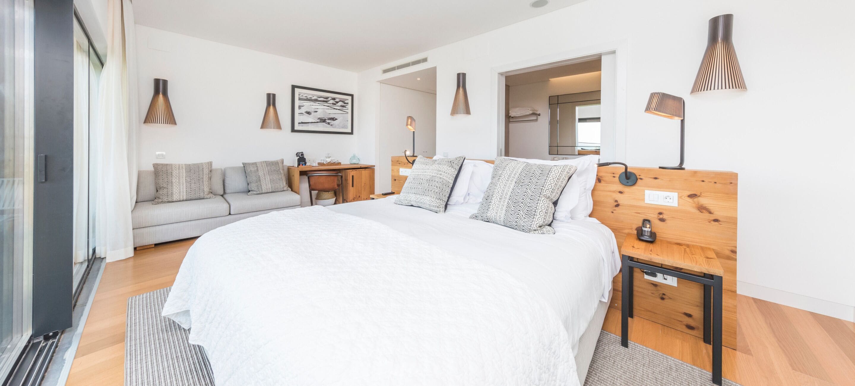 Quarto moderno com cama grande, mesa de cabeceira de madeira, escrivaninha e sofá.