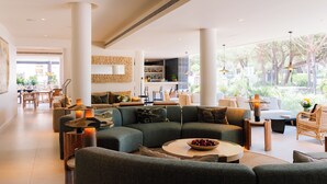 A spacious living area with a sectional sofa, a round coffee table with fruit, and a dining area with chairs and a table.