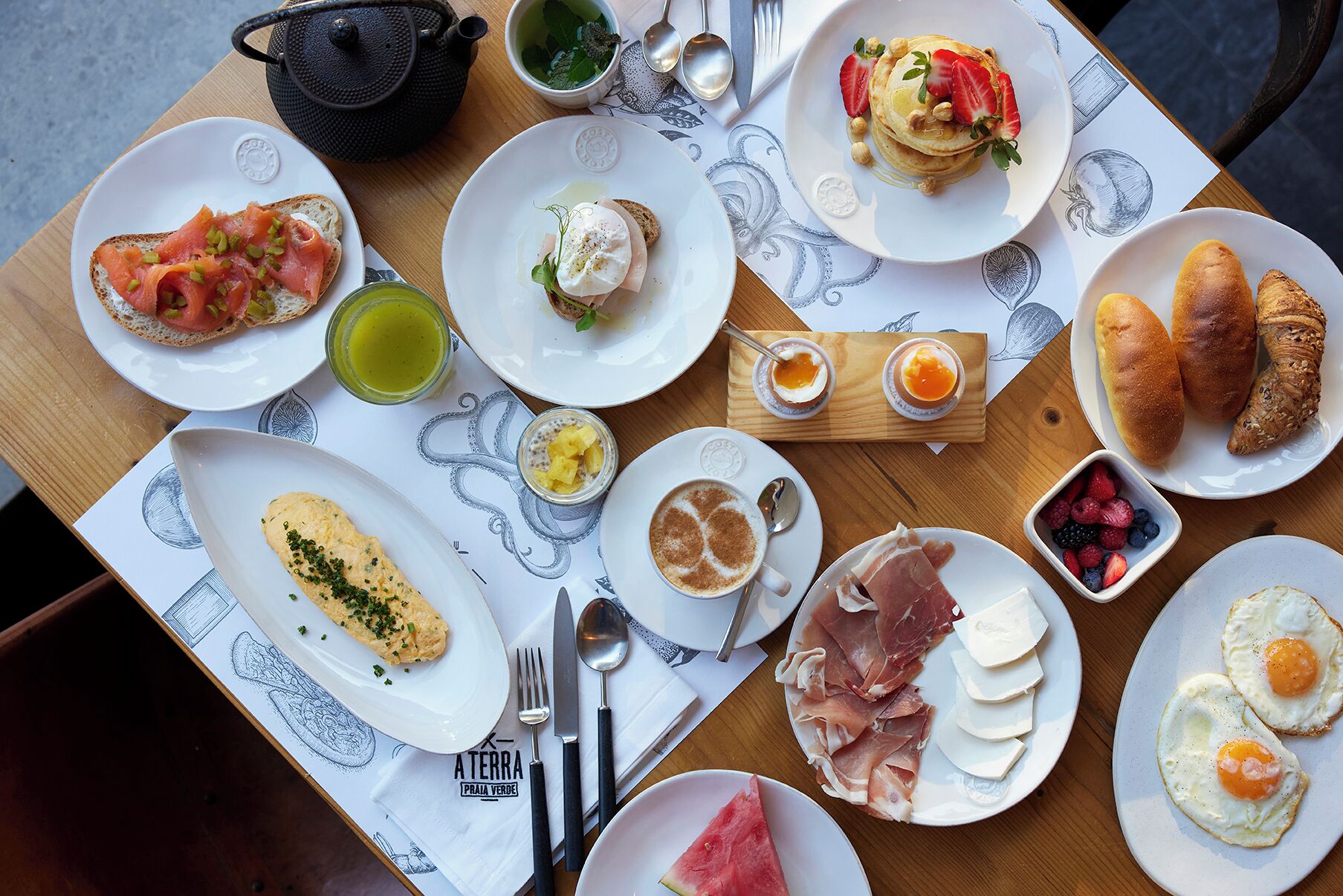 Una mesa servida con diferentes alimentos para el desayuno, incluyendo tostadas, huevos y pasteles.