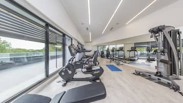 Un gimnasio moderno con máquinas de cardio, equipo de levantamiento de pesas y amplias ventanas con vistas a zonas verdes.