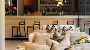 A modern living room with a sofa adorned with patterned cushions, a bar area with a counter and seating, and a large window providing natural light.