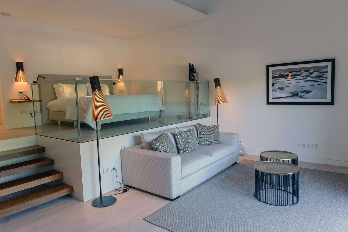 A modern hotel room with a glass-enclosed bed, a white sofa, and a framed picture on the wall.