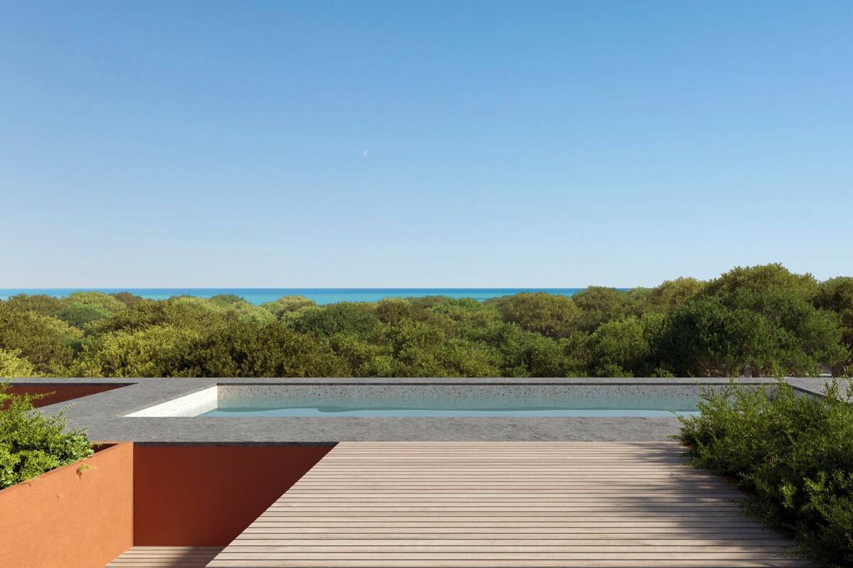 A rooftop pool with a wooden deck, surrounded by dense greenery and a clear view of the ocean.