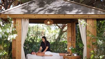 Um gazebo de madeira com teto inclinado, uma mesa de massagem e alguém oferecendo uma massagem.