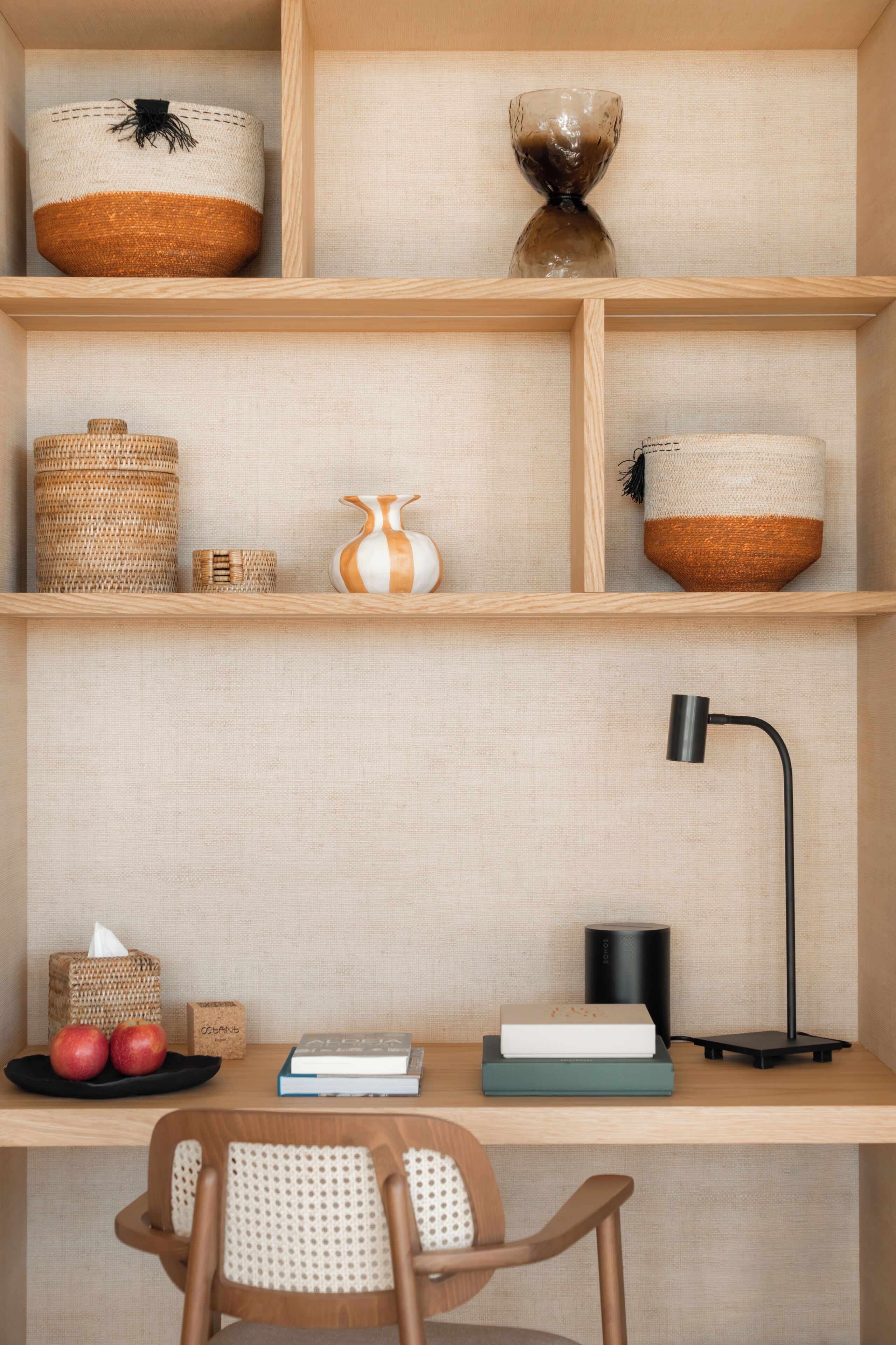 A wooden desk with a woven chair, a black lamp, and various decorative items including baskets and a vase.