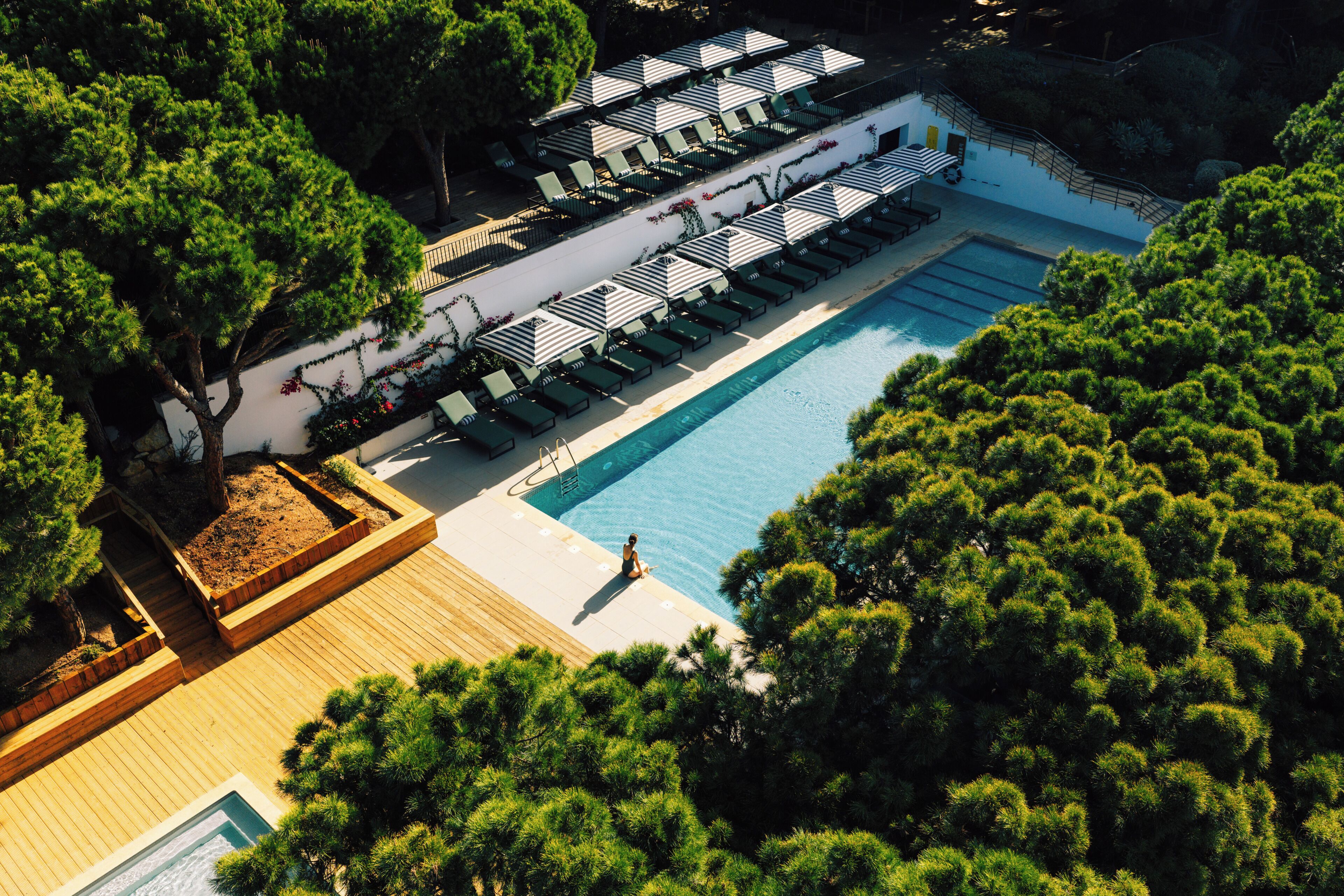 An aerial view of a resort with a swimming pool, sun loungers, and a wooden deck.