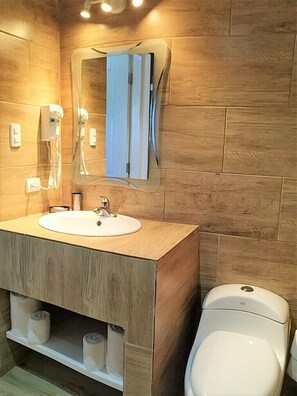 Uma casa de banho com uma cómoda de madeira, uma pia, um espelho, um secador de cabelo e uma sanita.