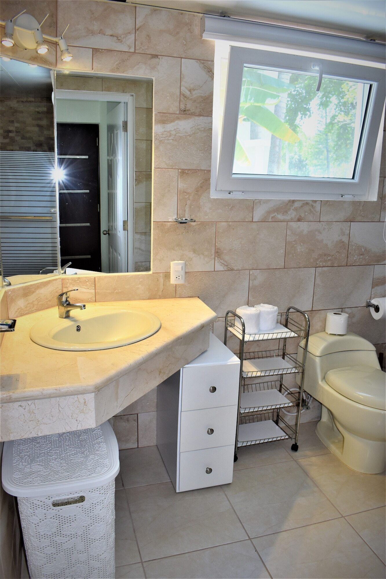 A bathroom with a sink, mirror, toilet, and a window.