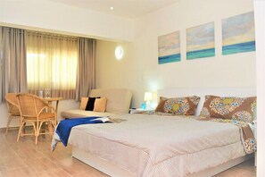 Quarto de hotel com uma cama, uma cadeira, uma mesa e um abajur. Há três quadros na parede.