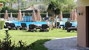A pool area with lounge chairs and umbrellas, a pool, and a view of the surrounding landscape. - Pegasus Hotel (Corfu)