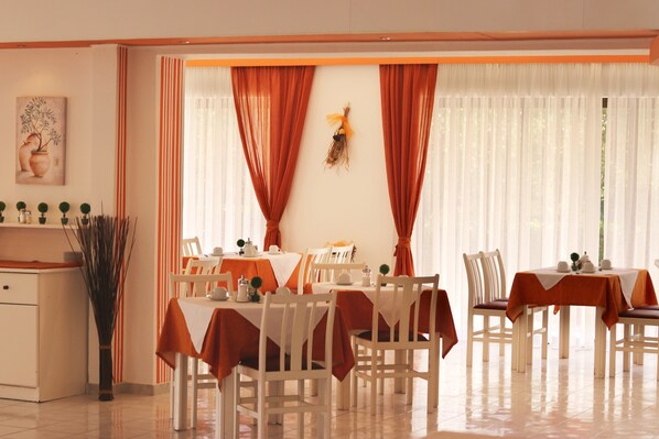A dining area with tables set for four, white chairs, and orange tablecloths. - Pegasus Hotel (Corfu)