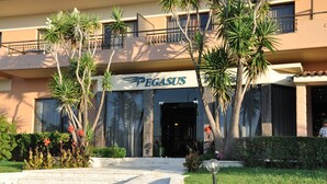 A hotel entrance with a sign reading "PEGASUS," surrounded by palm trees and a well-maintained garden. - Pegasus Hotel (Corfu)