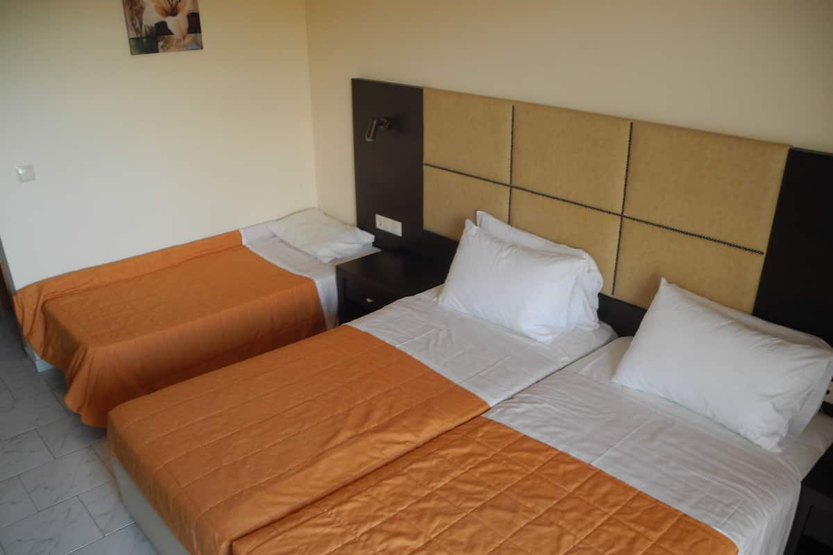 Habitación de hotel con dos camas individuales, cada una con colcha naranja y almohadas blancas.