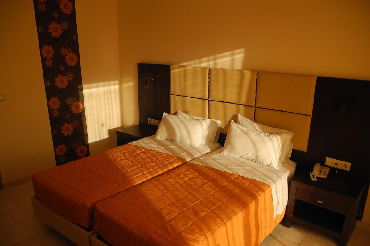 A double bed with a quilted orange bedspread, a headboard with a grid pattern, and a bedside table with a telephone.