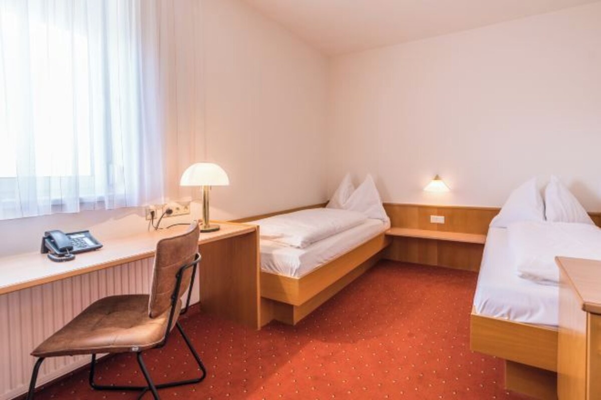 A hotel room with a desk, chair, two beds, a lamp, and a phone.