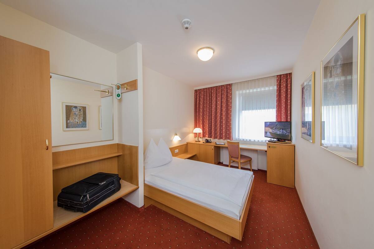A hotel room with a bed, a desk, a chair, a television, and a wardrobe.