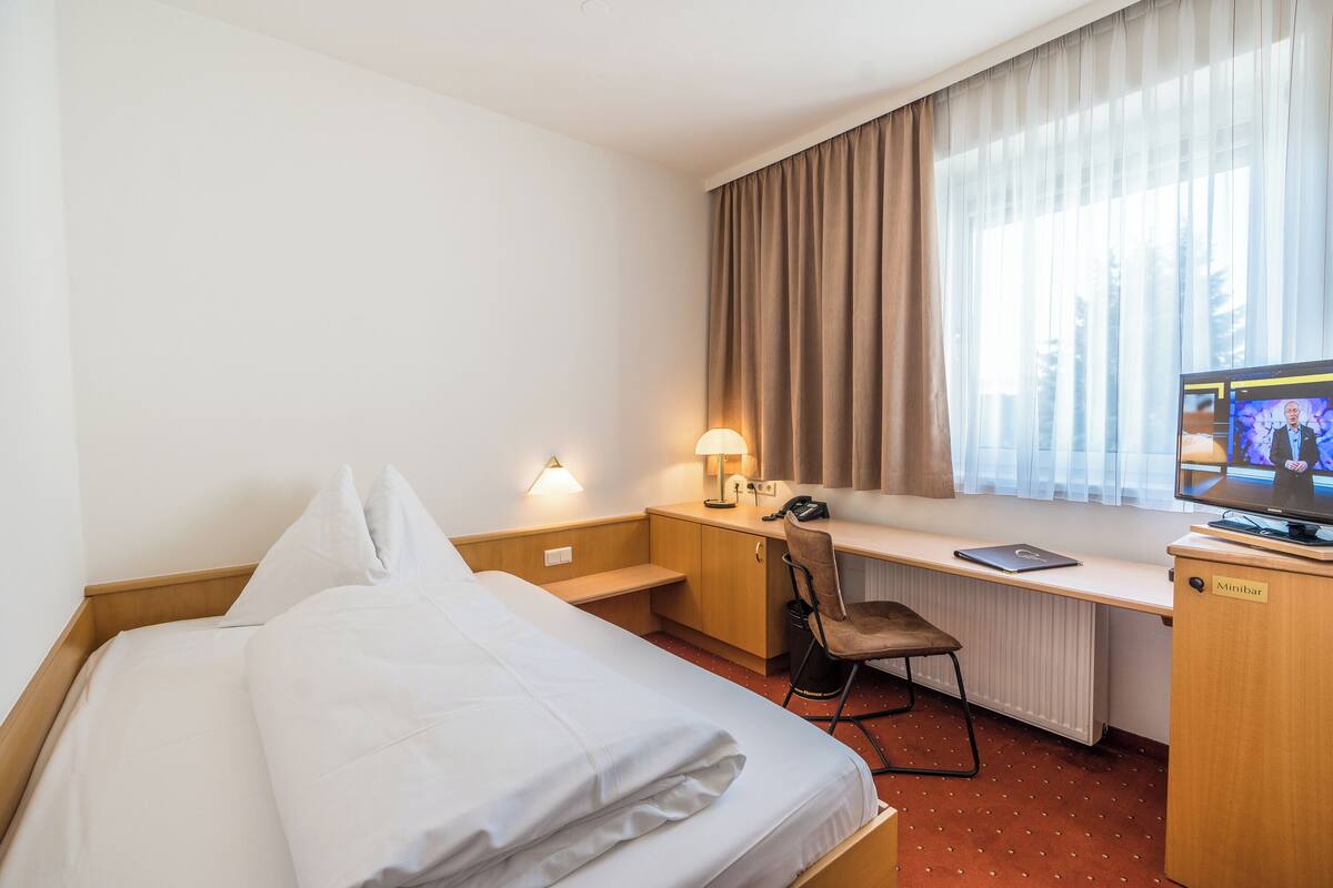 A hotel room with a bed, desk, chair, and a television.