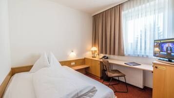 A hotel room with a bed, desk, chair, and a television.