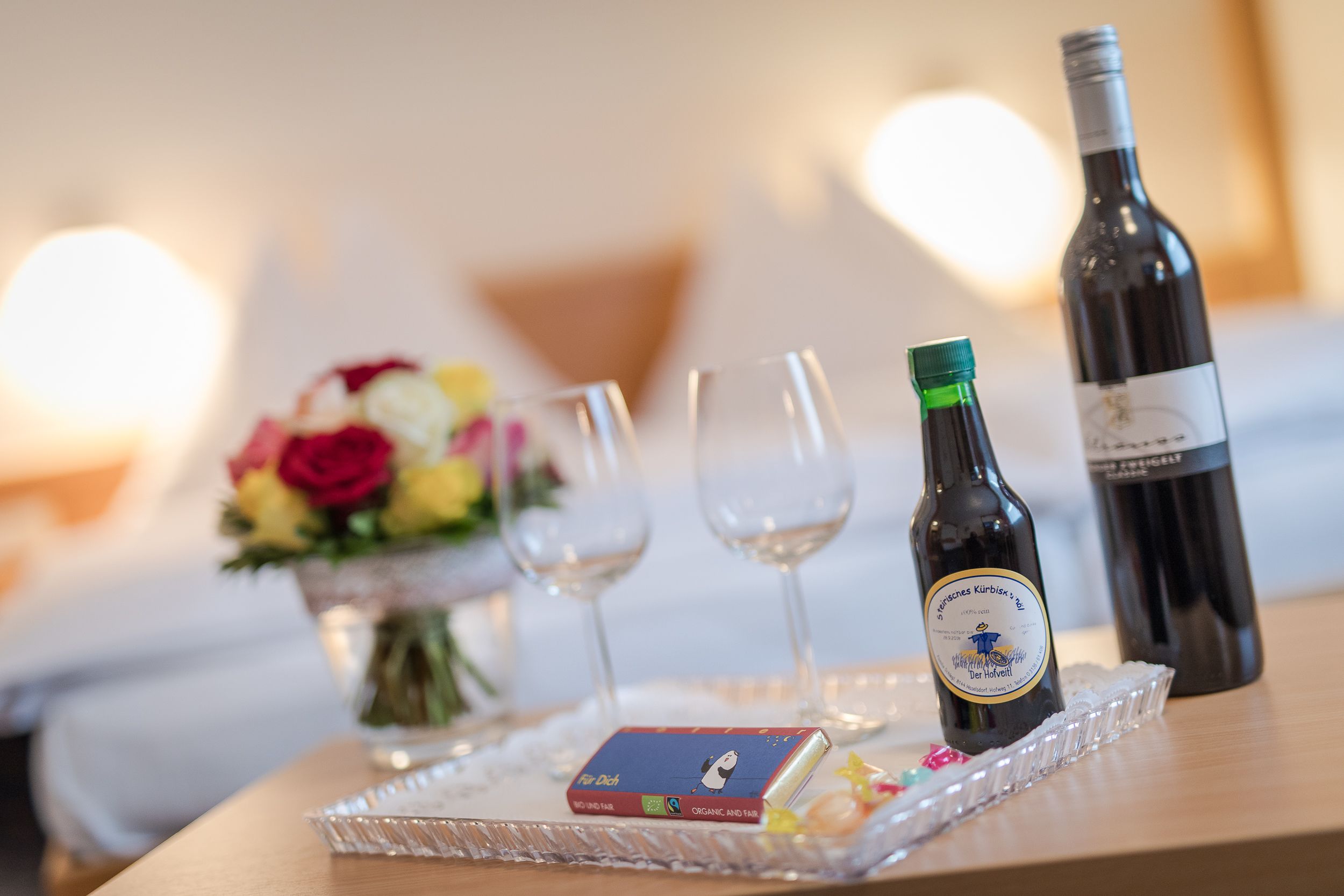 Une table avec une bouteille de vin, deux verres, une petite boîte et un vase de fleurs.