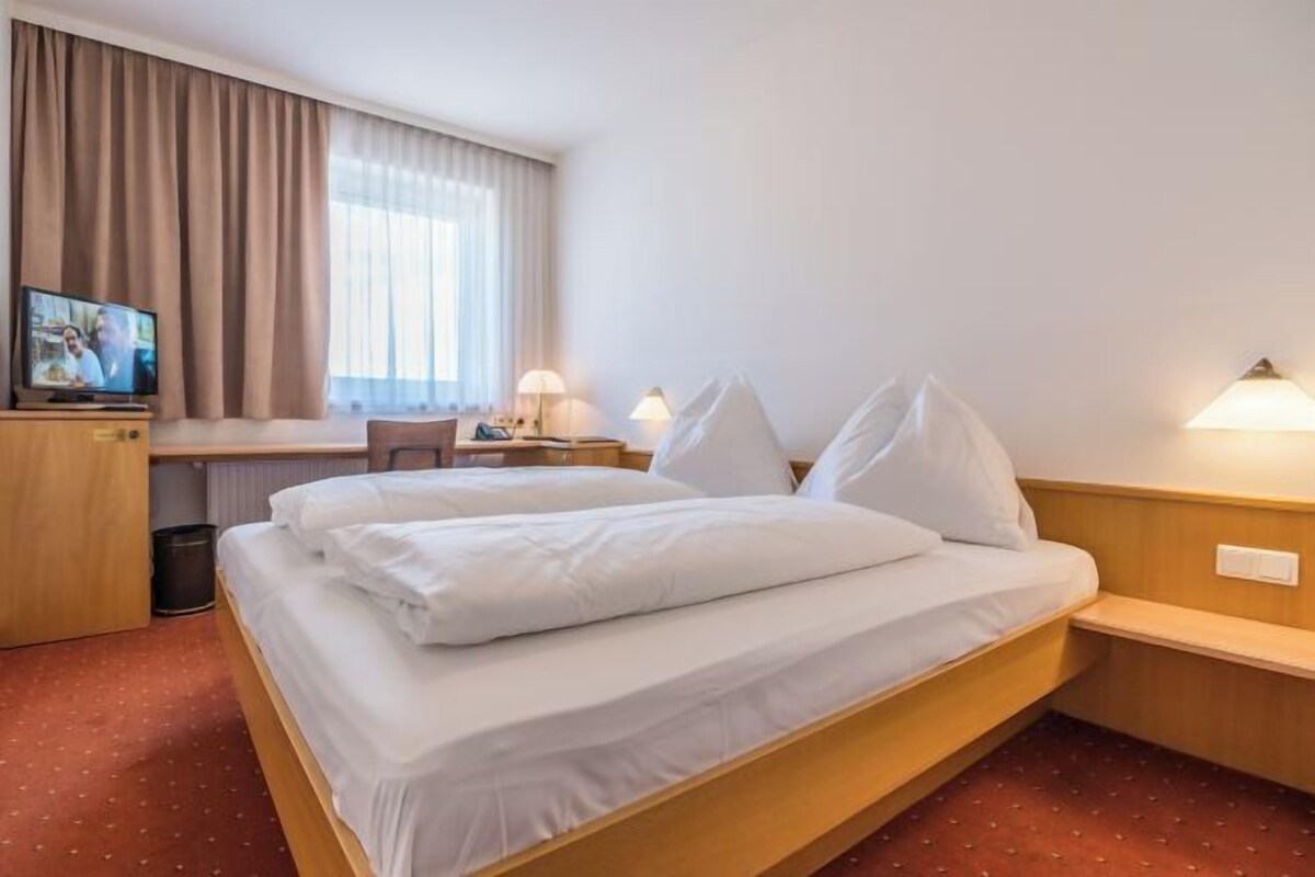 A hotel room with a bed, a desk, a TV, and a lamp.