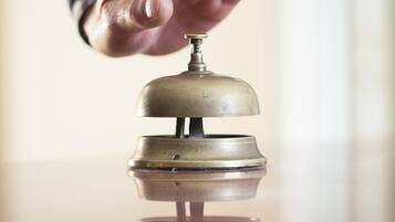 A hand reaching for a brass bell on a reflective surface.