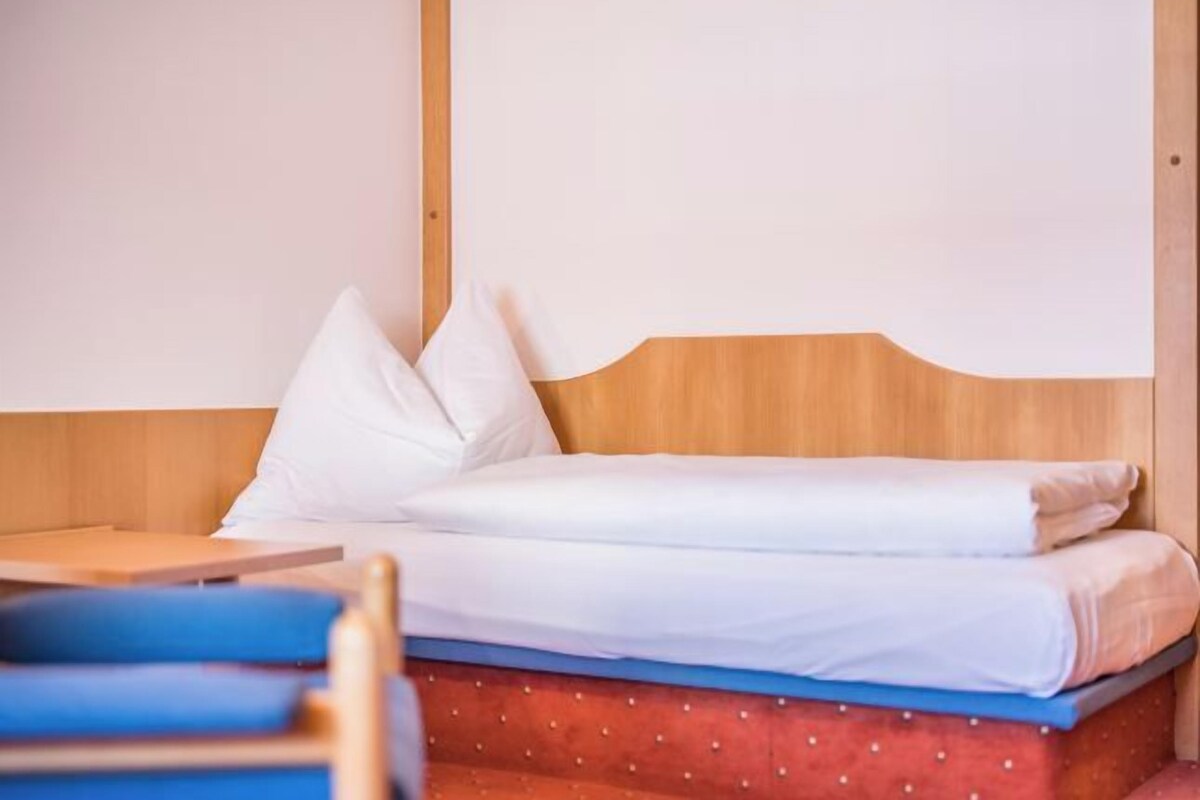 A single bed with white bedding, a wooden headboard, and a red mattress cover.