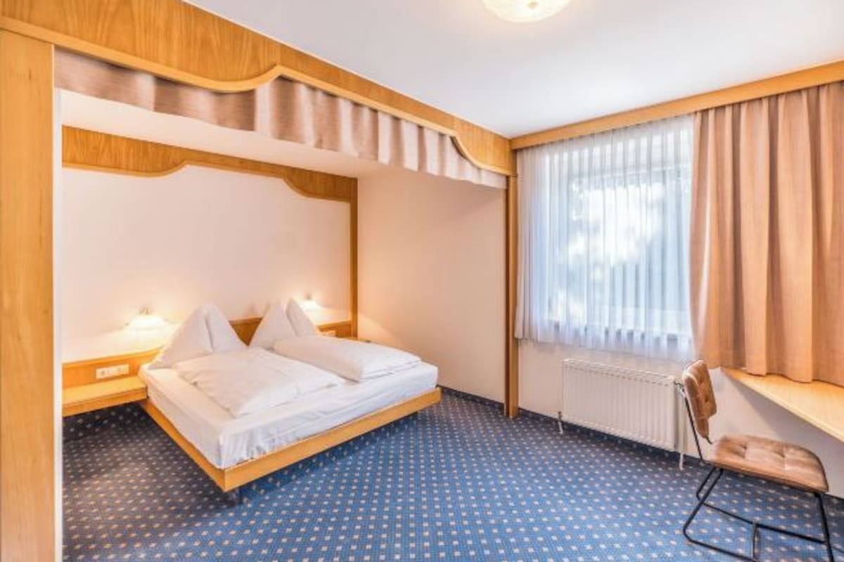 A hotel room with a bunk bed, a desk with a chair, and a window with curtains.