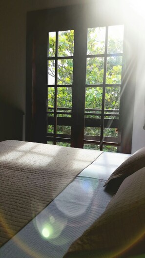 Ein Zimmer mit einem Bett, einem Fenster mit Blick auf Grünflächen und einer Tür.
