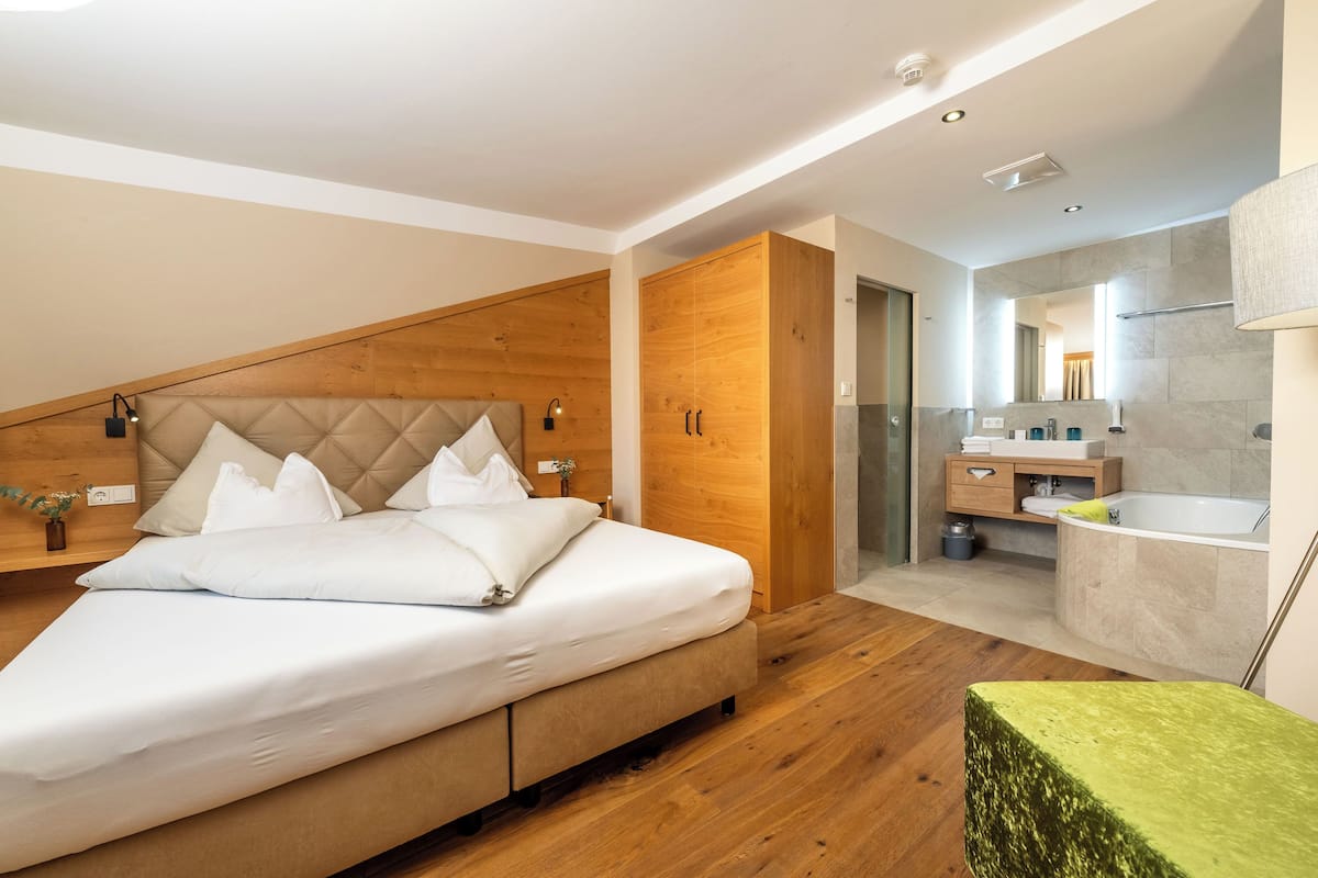Een moderne slaapkamer met een bed, een houten garderobe en een badkamer met bad en wastafel.