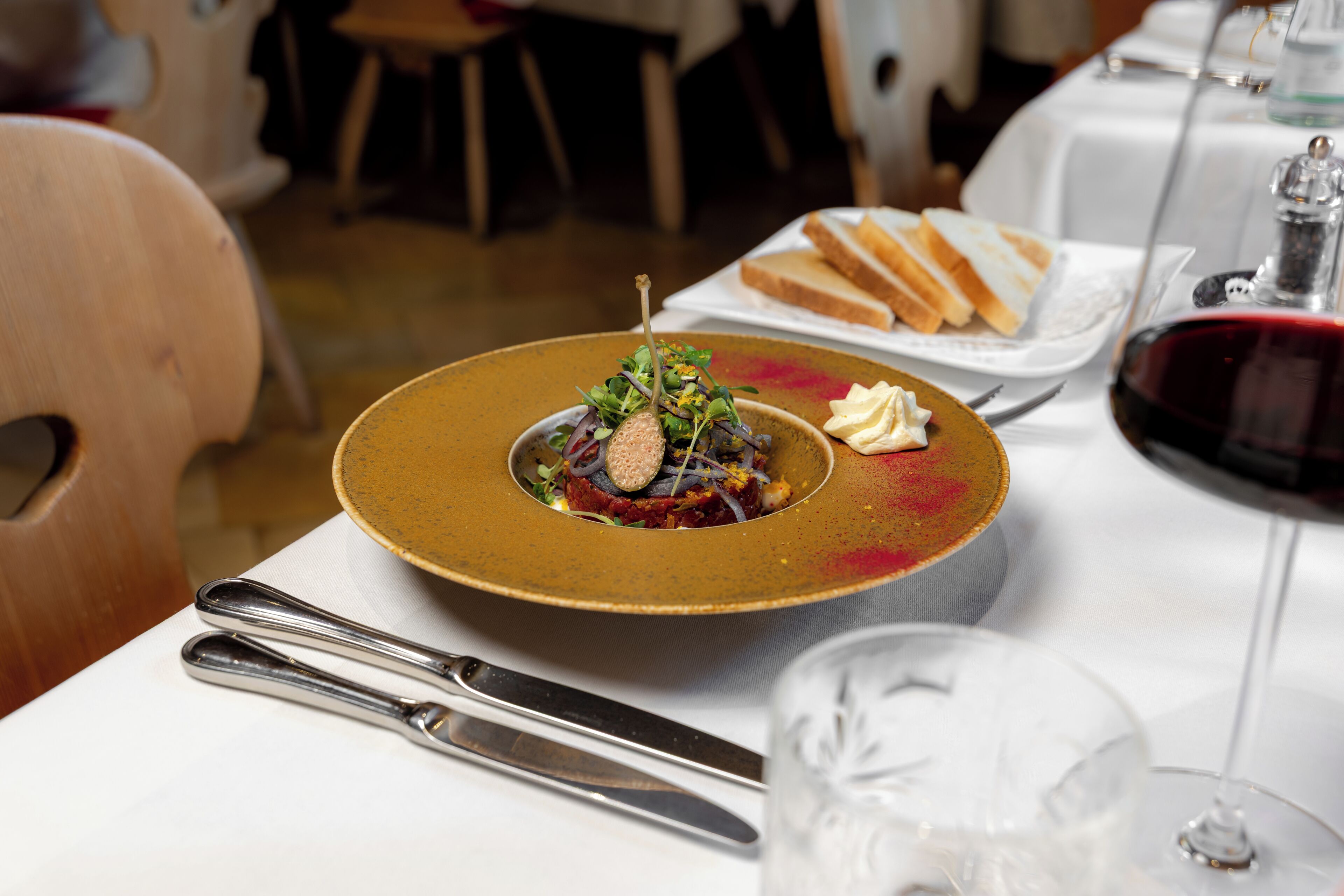 Une table à manger avec une assiette de nourriture, un verre de vin rouge et des couverts.