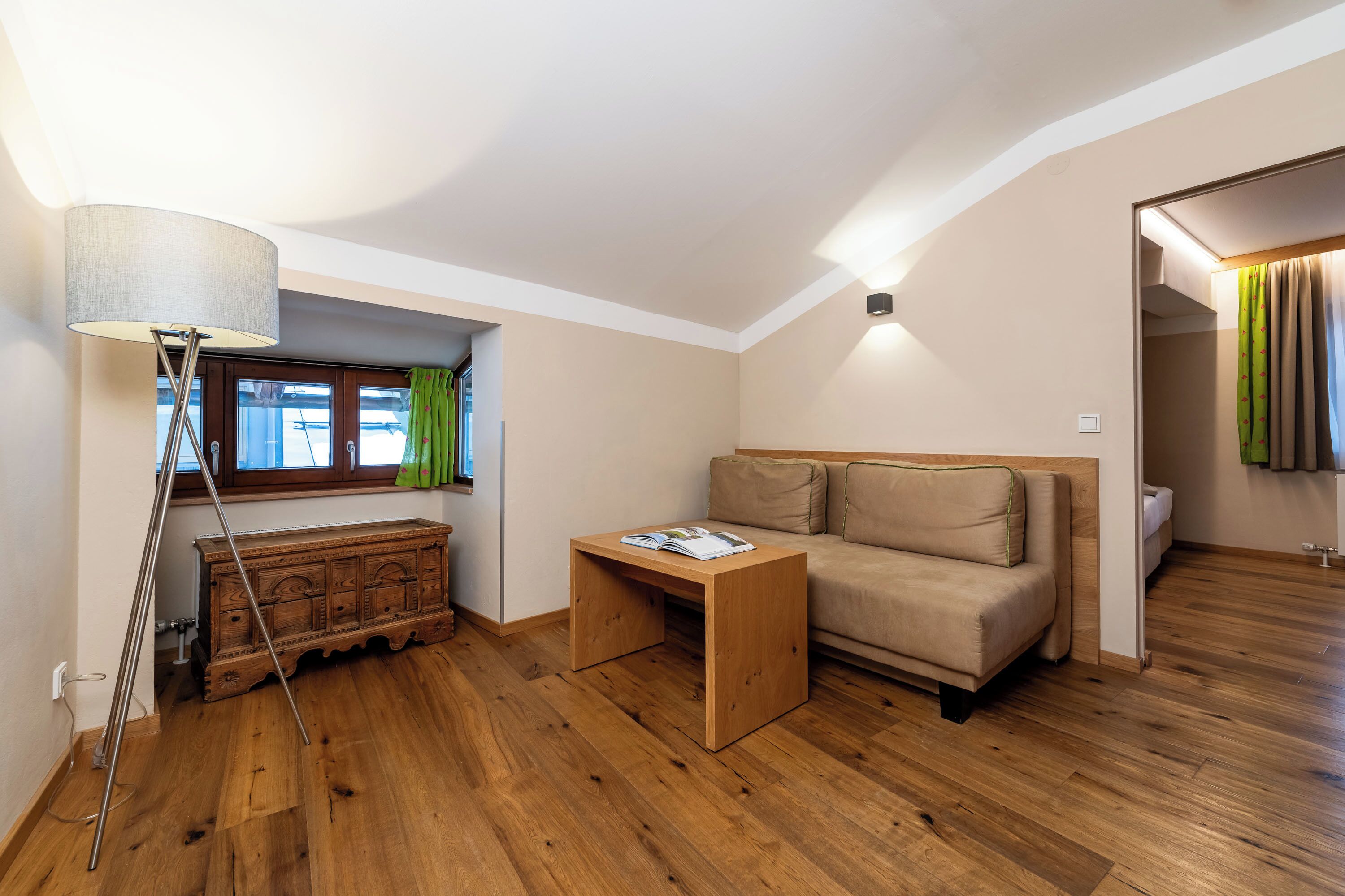 A modern living room with a wooden floor, a sofa, a coffee table, a lamp, and a window with curtains.