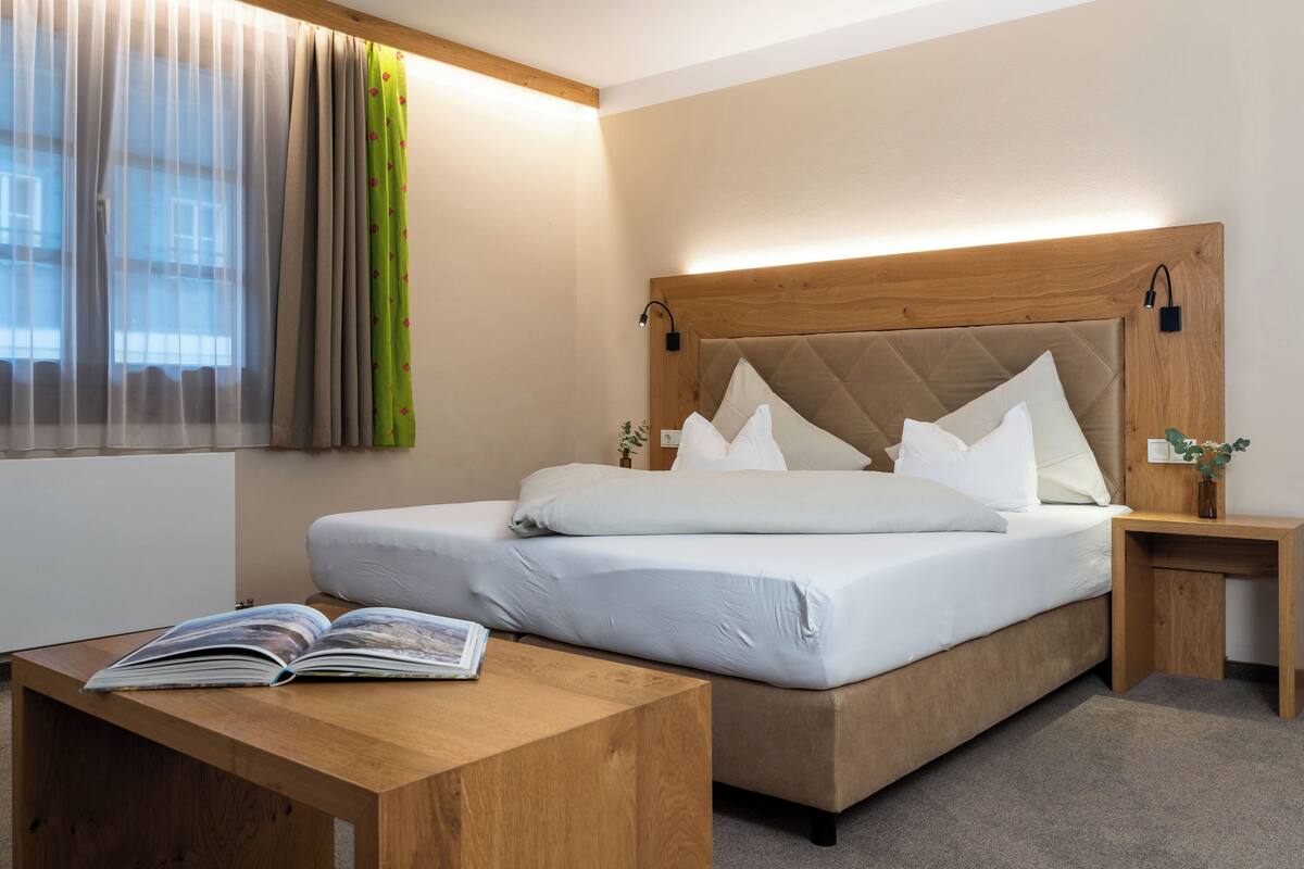 Een netjes ingerichte hotelkamer met een bed, nachtkastje en een raam met dunne gordijnen.