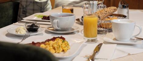 Una mesa de desayuno con huevos revueltos, tostadas, jugo y café.