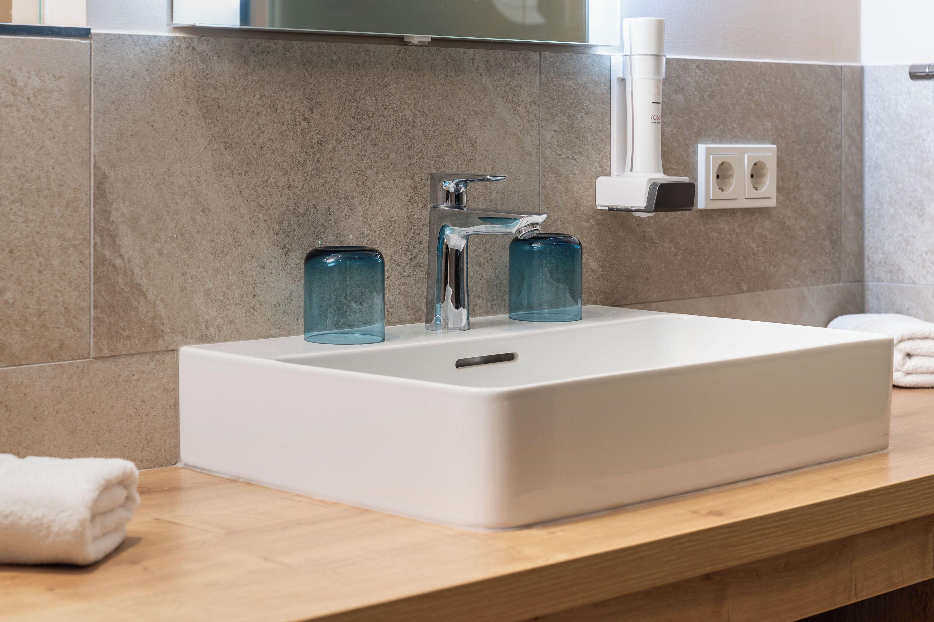 Un baño moderno con un lavabo blanco, dos frascos de vidrio y una toalla en la encimera.
