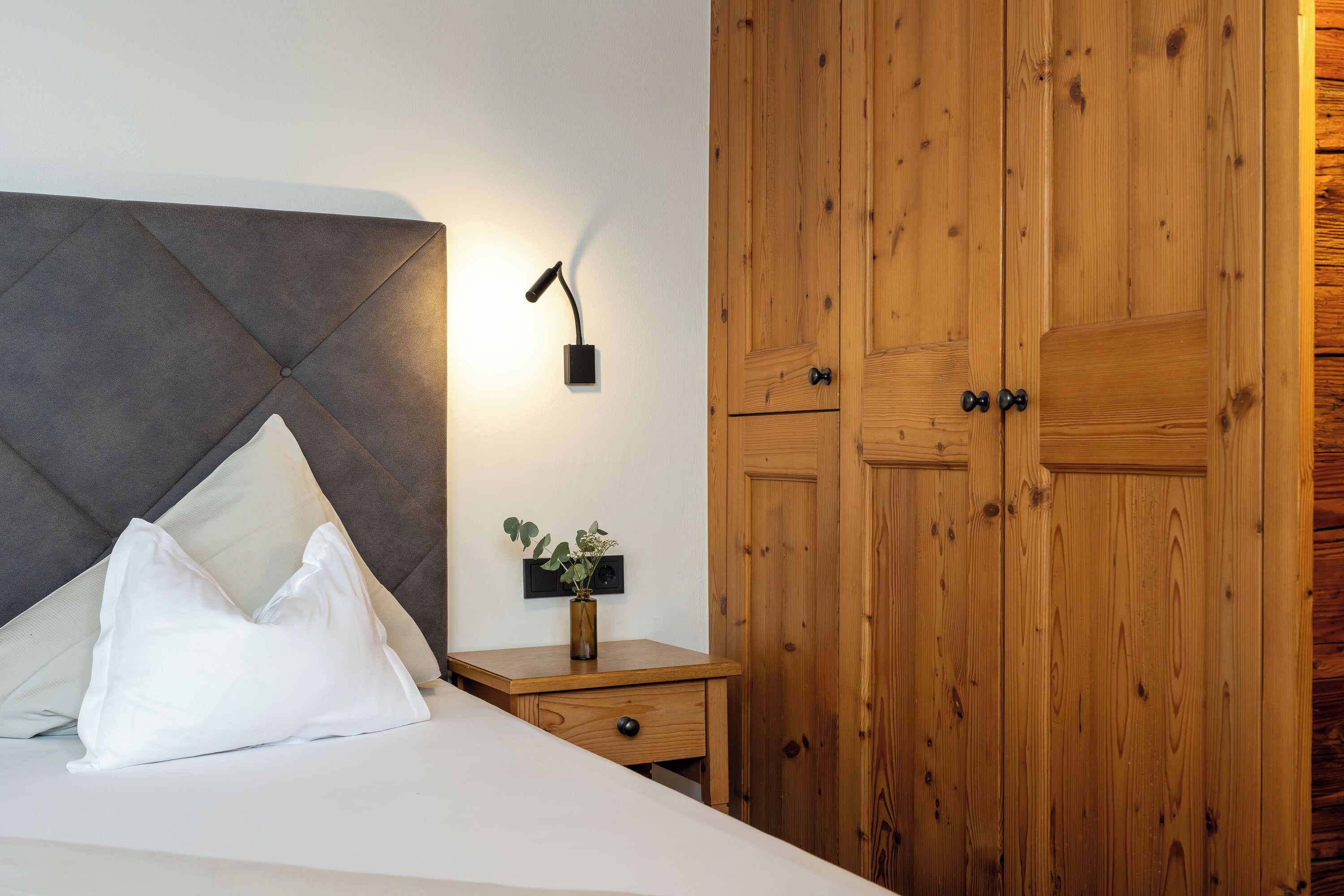 A bedroom with a bed, a nightstand with a vase, and wooden wardrobe doors.