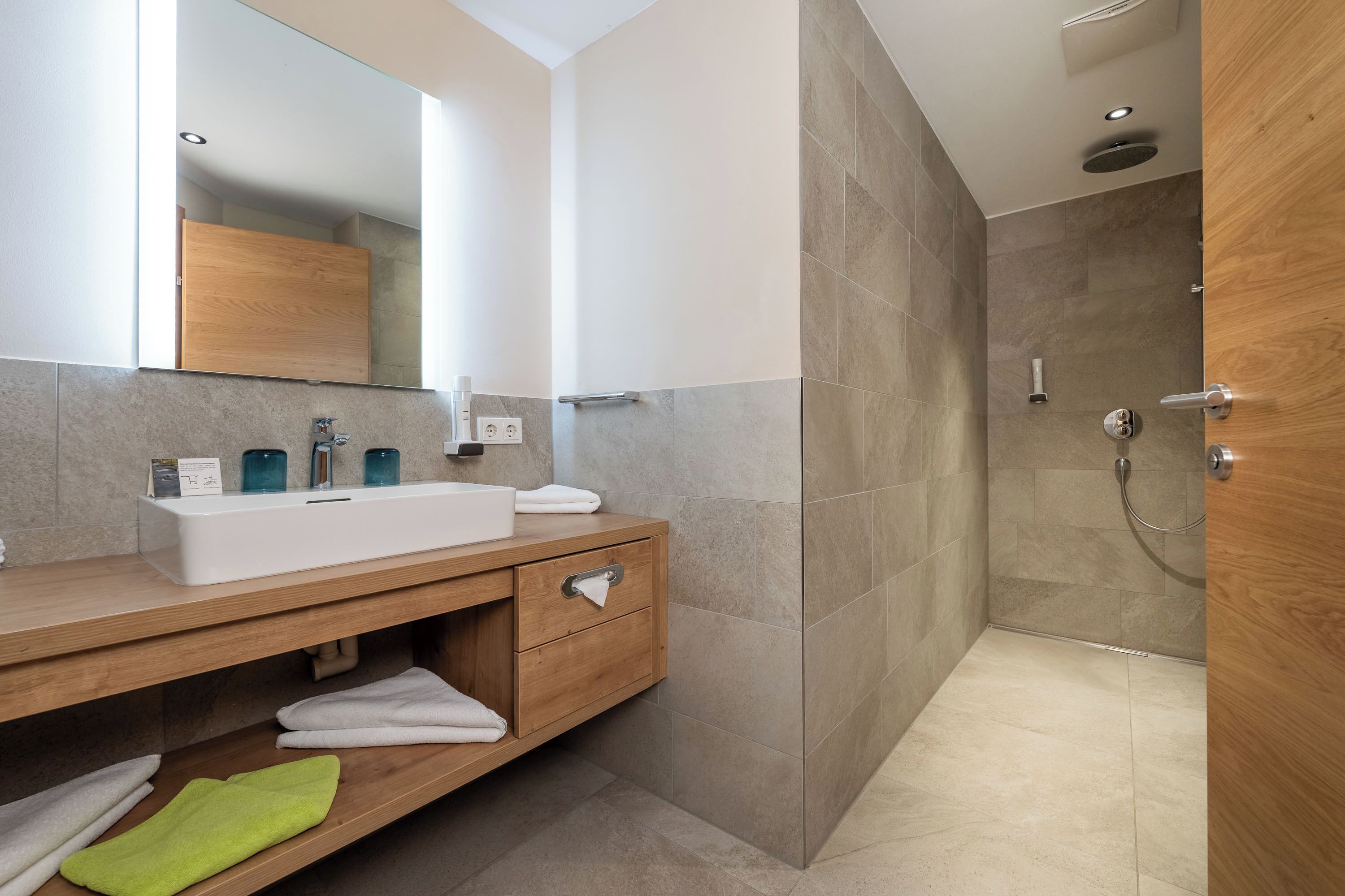 Un baño moderno con tocador de madera, un espejo grande y zona de ducha.