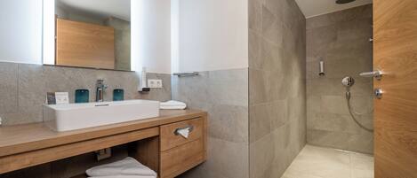 Un baño moderno con tocador de madera, un espejo grande y zona de ducha.