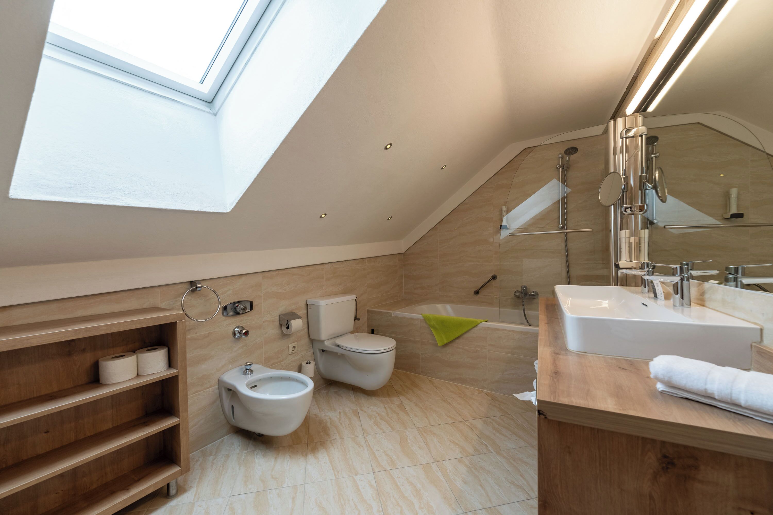 A modern bathroom with a skylight, a bidet, a bathtub, and a vanity with a mirror.