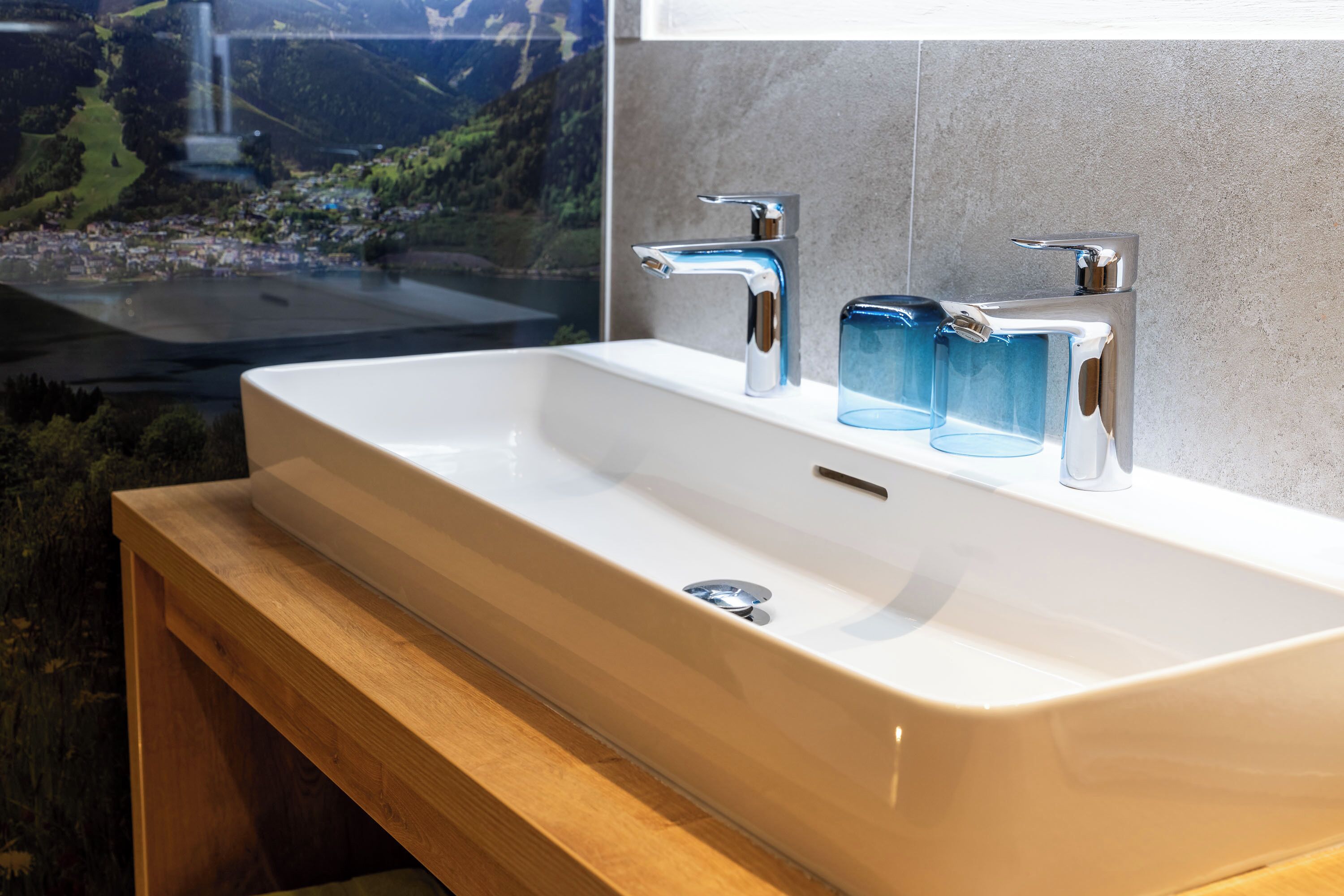 A bathroom with a white sink, two chrome faucets, and three blue glass soap dispensers.