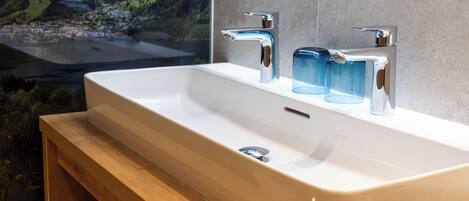 A bathroom with a white sink, two chrome faucets, and three blue glass soap dispensers.