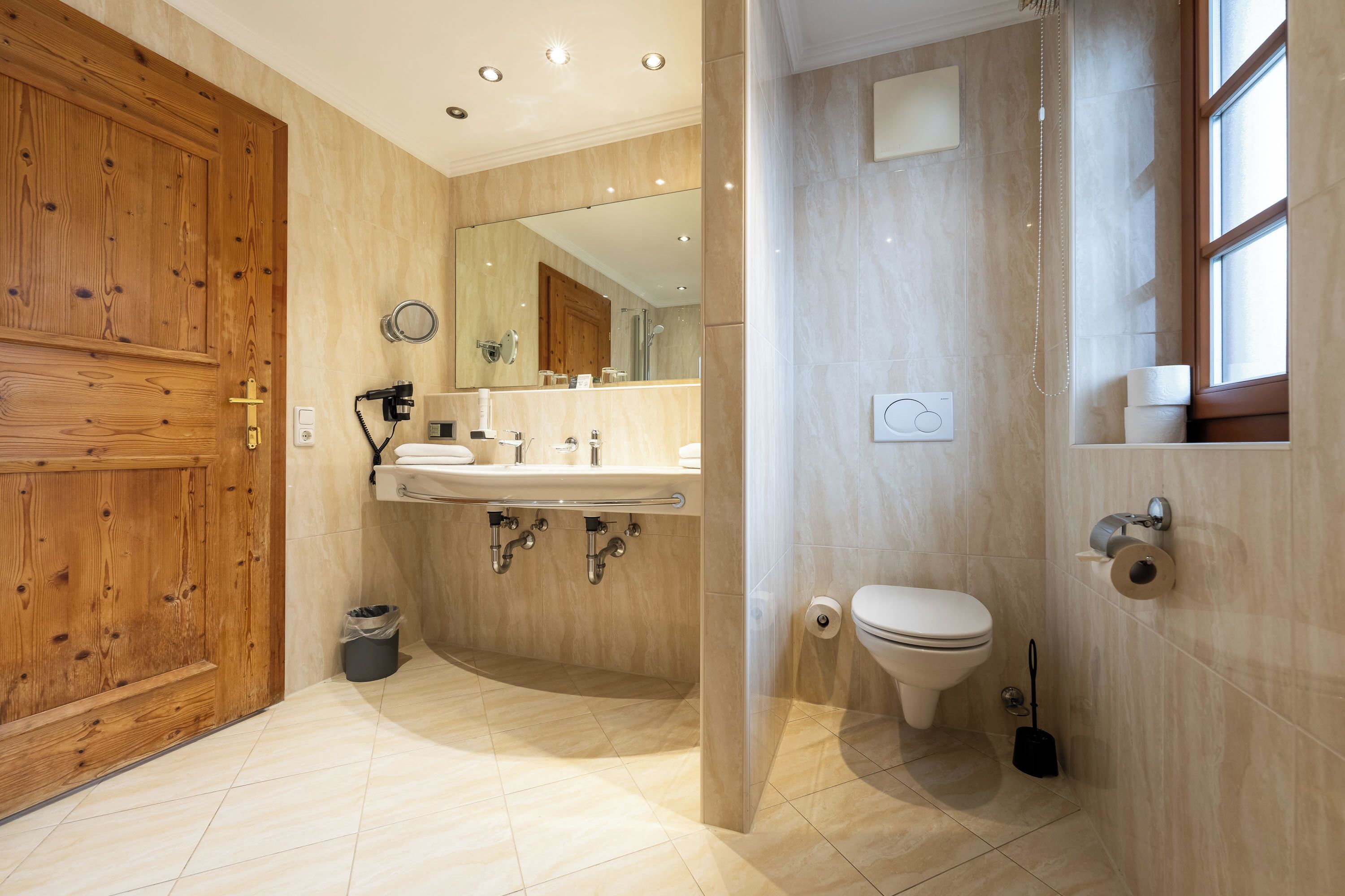 A modern bathroom with a wooden door, a sink with a mirror, a toilet, and a shower area.