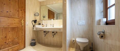 A modern bathroom with a wooden door, a sink with a mirror, a toilet, and a shower area.