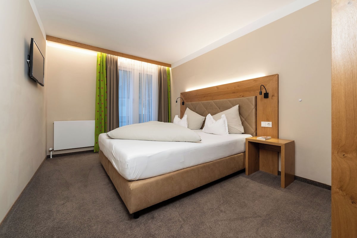 Een hotelkamer met een bed, nachtkastje en een aan de muur bevestigde televisie.