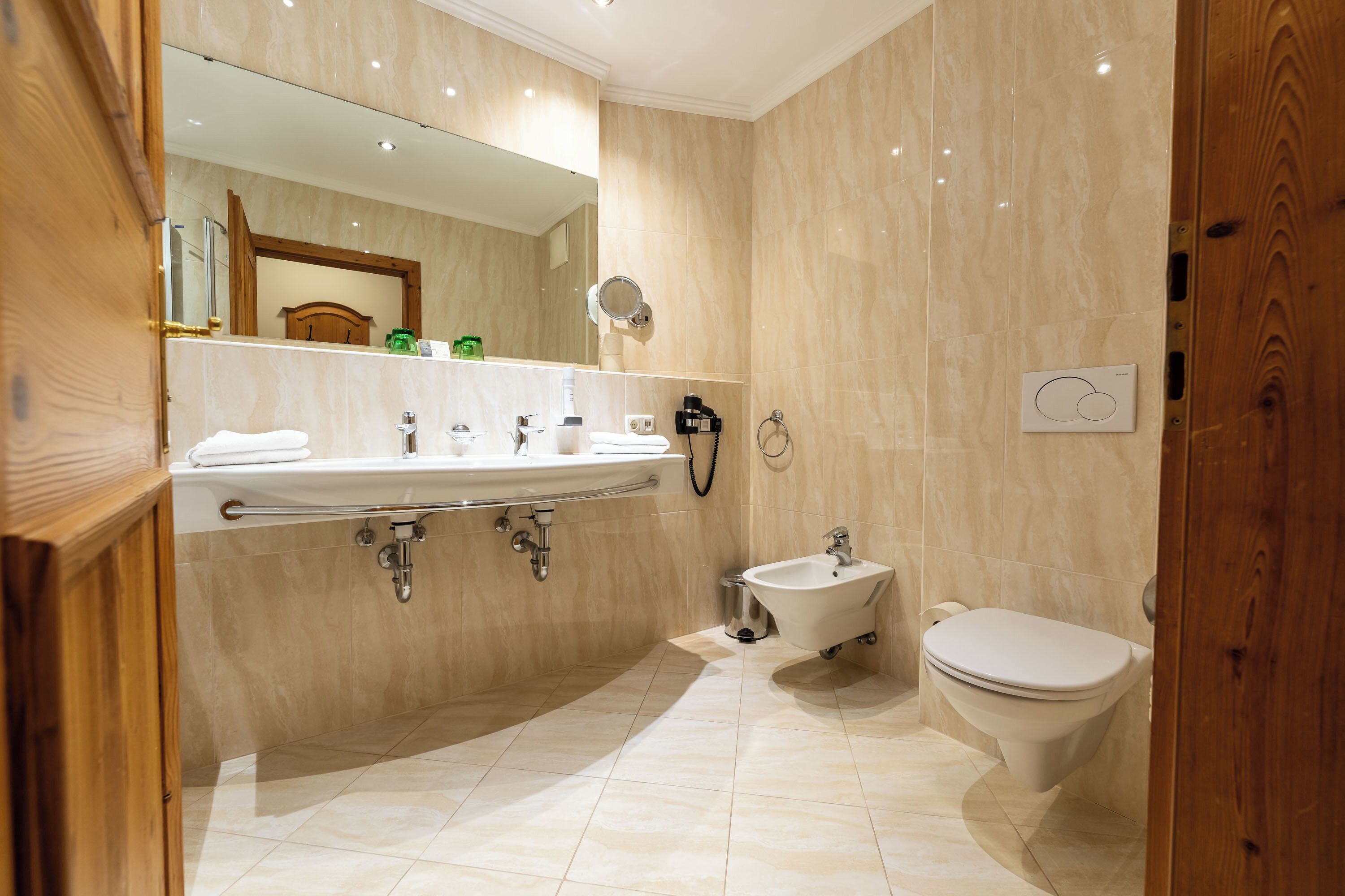 A modern bathroom with a large mirror, a sink, a bidet, and a toilet.