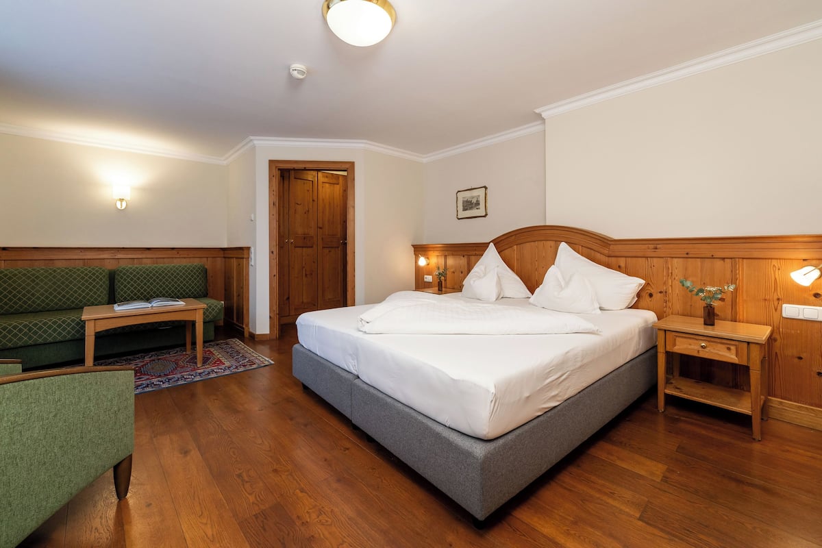 Een slaapkamer met een bed, een groene bank, een houten nachtkastje en een kleine tafel.
