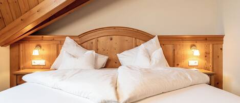 Una cama bien hecha con sábanas blancas y almohadas, cabecera de madera y dos lámparas de noche.