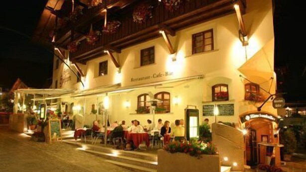 Un restaurant doté d’une terrasse, une enseigne indiquant « Restaurant-Café-Bar » et un escalier menant à l’entrée.